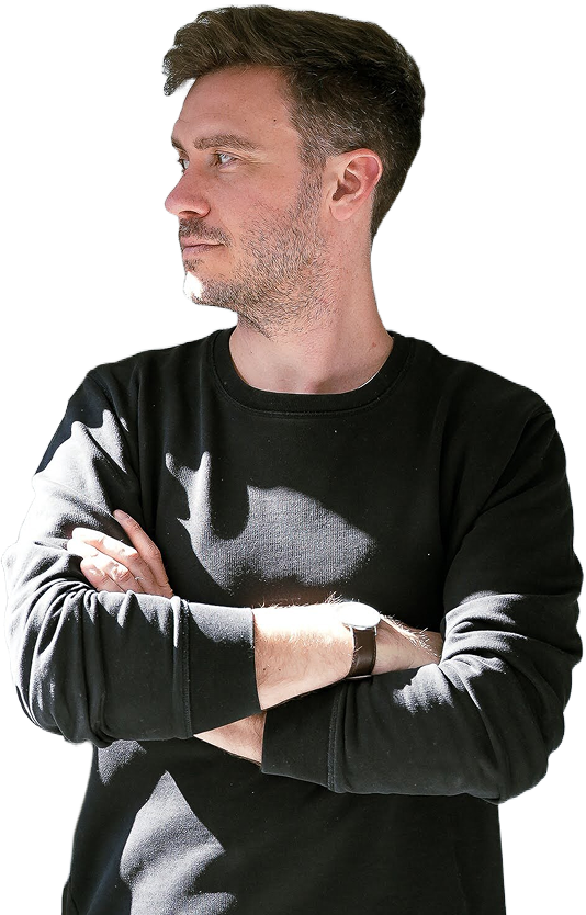 Philipp Kaiser im schwarzen Pullover mit verschränkten Armen, im Sonnenlicht zur Seite blickend